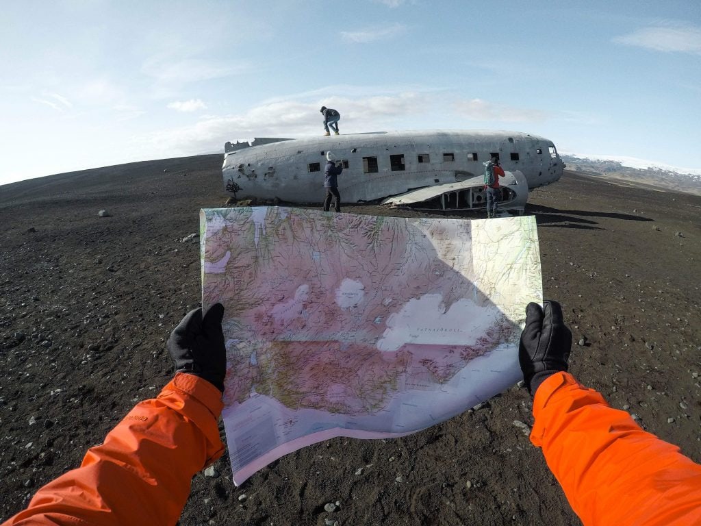First-person view of hands holding a map with an old airplane fuselage in the background.