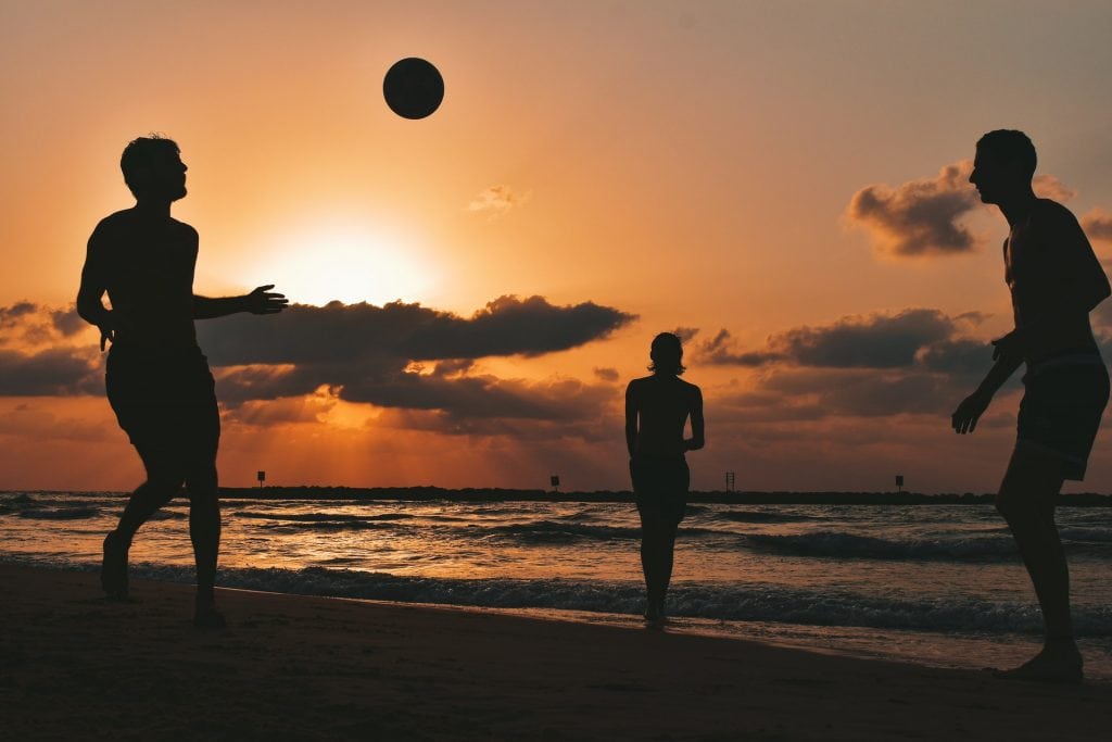 Silhouette of two men and a woman playing football on the beach at sunset.