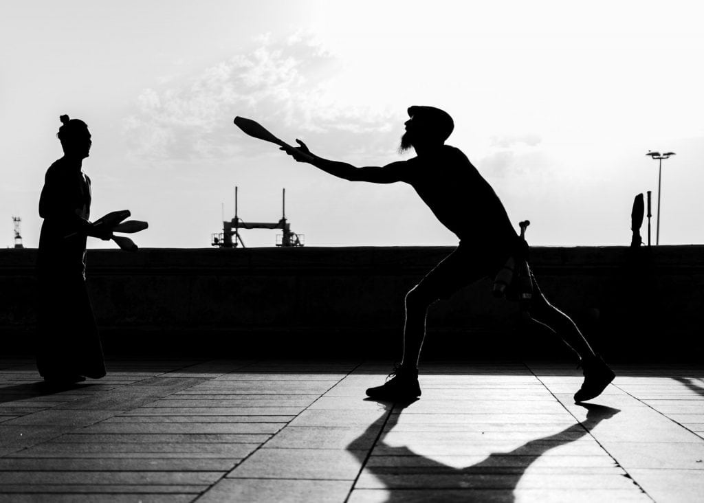 Black and white silhouette of two men juggling.