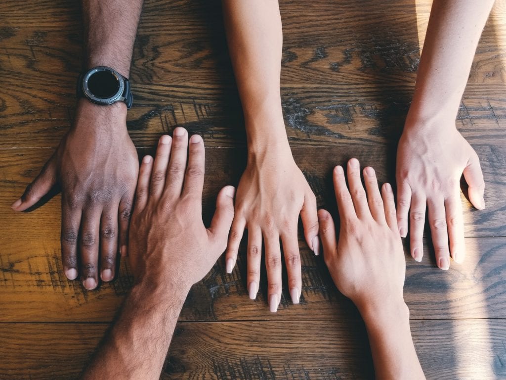 Five humans hands of different genders and races laid down on table.