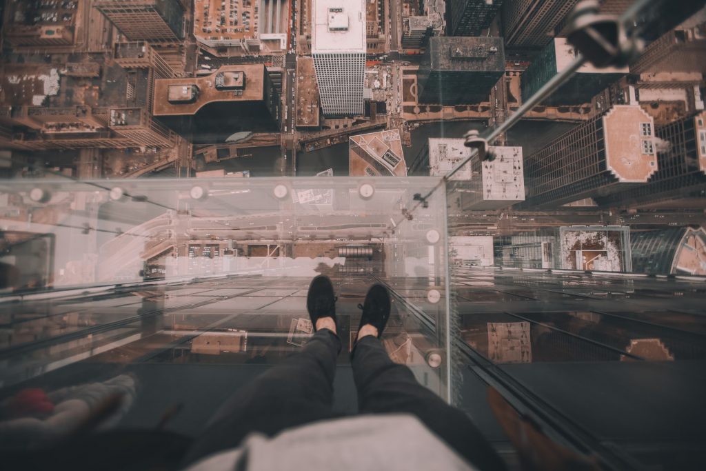POV of man standing on a glass platform on a high rise building, looking down.