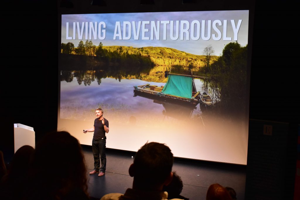 alastair humphreys on stage in front of a screen that says 'living adventurously'