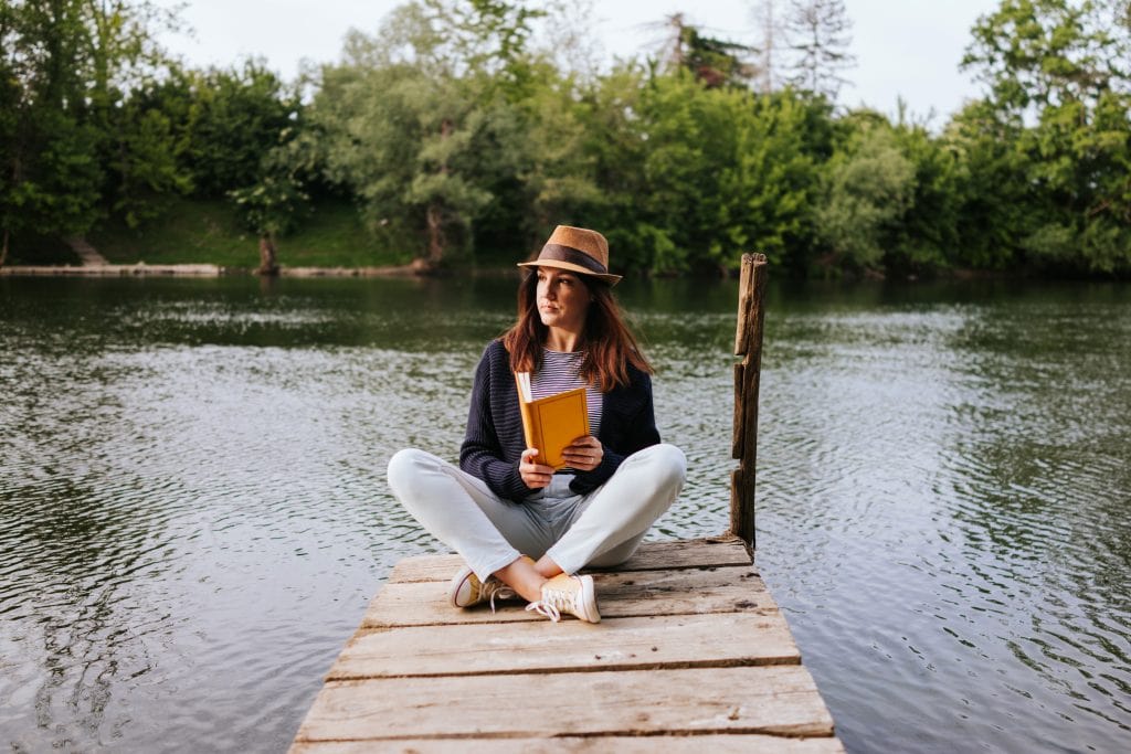 young woman on a river pier reading book