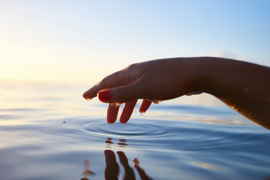 fingertips dipping into calm water