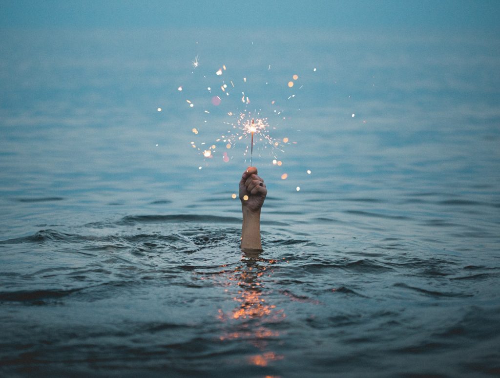 hand holding a sparkler from body of water