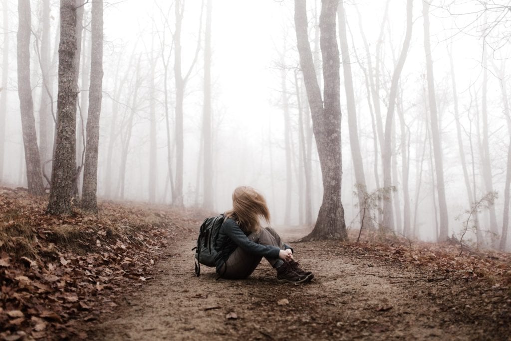 woman sitting on forest floor in misty forest alone