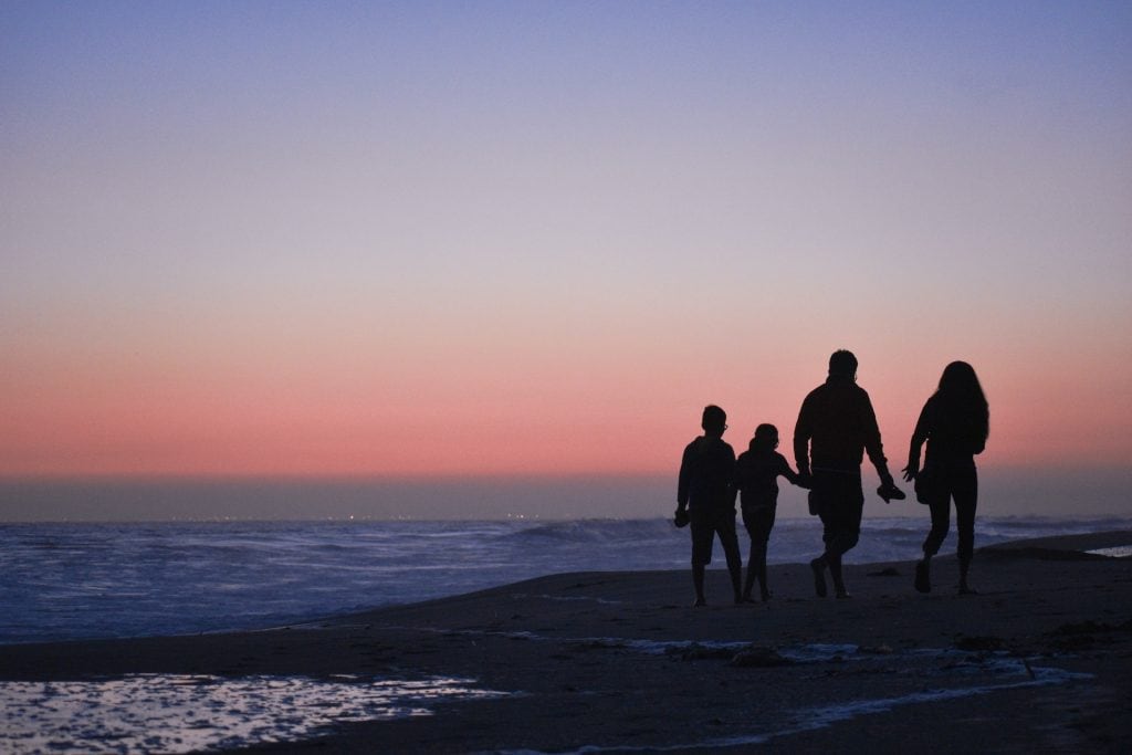 silhouette of man and woman with two children on the beach