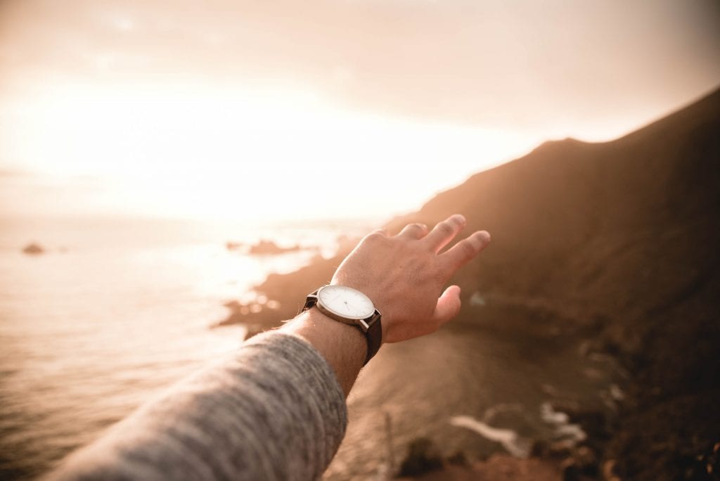 person's left arm with watch on wrist with sunset over ocean