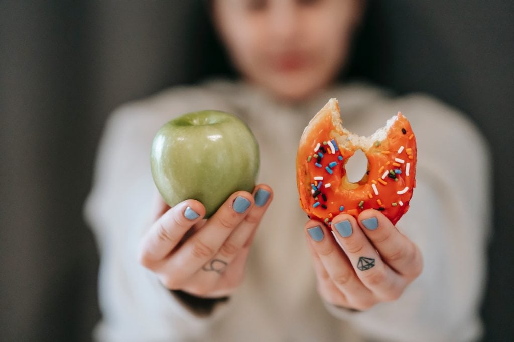 woman holds apple in one hand and donut in the other